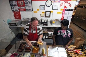 Owner Carl Baker and employee Nakita McGruder prepare a hot dog for a customer Tuesday at the Hot Dog Man on Drummond Street. (Justin Sellers/The Vicksburg Post)
