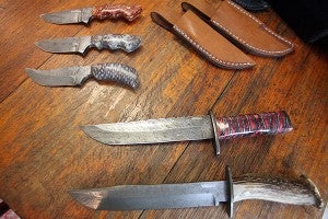Several of the knives made by blacksmith Bill Mangum are displayed Thursday on his kitchen table. Many of the knives Mangum makes have handles created from pine cones, magnolia pods, firewood, and other natural material found in Vicksburg. "I've never made two that look exactly the alike," he said. (Justin Sellers/The Vicksburg Post)